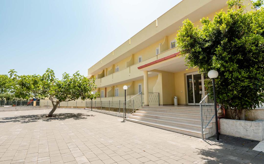 Edificio giallo soleggiato, alberi verdi, atmosfera serena e accogliente.