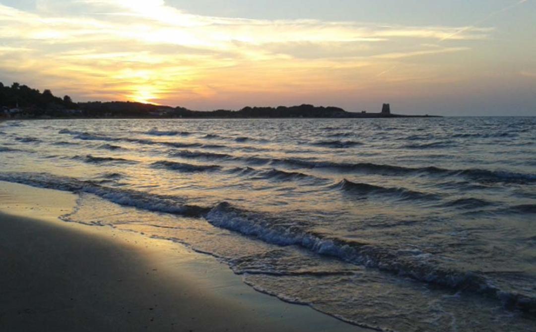 Tramonto sereno su mare calmo, onde delicate e cielo dipinto di arancio.
