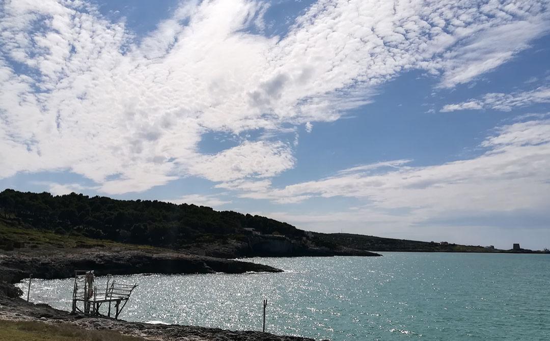 Mare turchese, cielo azzurro e nuvole soffici sopra una costa rocciosa.